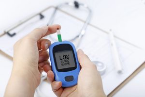 hand holding blood glucose meter measuring blood sugar the background is stethoscope and chart file